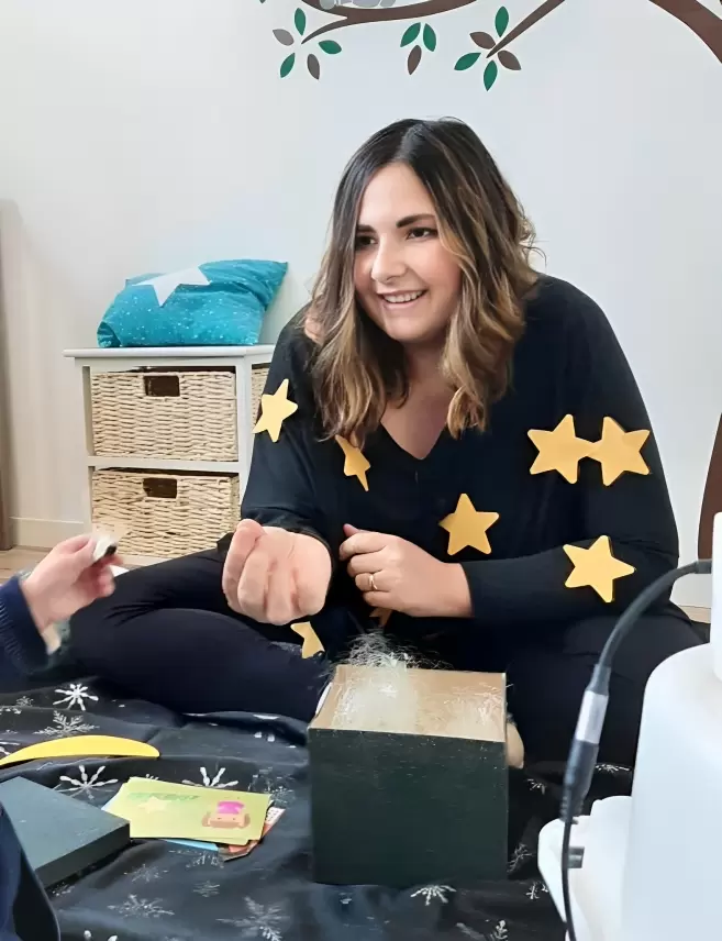 Photo d'Anaïs des instants de bonheur habillée d'un pull noir orné d'étoiles jaunes lors d'un atelier histoire enchantée sur le thème de l'espace